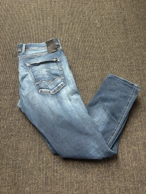 Replay anbass med slitningar - Snygga blå anbass jeans från Replay med klassisk femficksmodell och coola slitningar framtill. Jeansen har raka ben och kontrastsömmar samt en läderpatch bak i midjan. Perfekta för dig som gillar en avslappnad men trendig stil. Storlek 34 men sitter mer som w32.