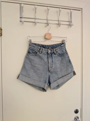 Högmidjade ljusblå jeansshorts - Snygga högmidjade jeansshorts i ljusblå denim med uppvikta benslut. Den är i storlek W26 eller XS