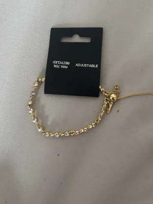Guldarmband med pärlor och justerbar kedja pilgrim - Snyggt armband i guldfärg med små vita pärlor längs hela bandet. Armbandet har en justerbar kedja med två små kulor i ändarna, vilket gör det enkelt att anpassa storleken. Helt nytt och oanvänt säljer även likadan i silver