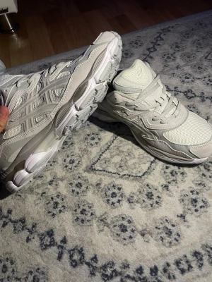 Vita Asics sneakers med mesh och skinn - Snygga vita sneakers från Asics med en chunky sula och detaljer i både mesh och skinn. Skorna har klassisk snörning och en sportig vibe som passar perfekt till streetwear. Diskreta loggor på sidan och bekväm passform.