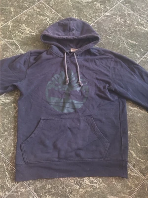 Mörkblå hoodie  - En snygg hoodie från timberland. Färgen är mörkblå och trycket är en nyans av mörkgrön. Skicket är okej. Storlek är S. Hör av dig vid fler bilder på defekter eller frågor!