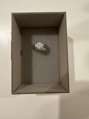 Silverfärgad ring med stor sten - Snygg silverfärgad ring med en stor, rund klar sten i mitten. Ringen har en enkel och stilren design som verkligen framhäver stenen. Perfekt för dig som gillar att sticka ut med dina accessoarer.