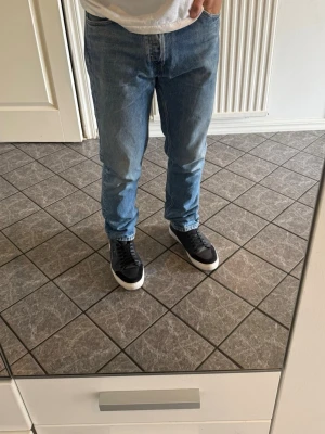 Ljusblå raka jeans herr - Säljer ett par ljusblå jeans med rak passform och klassisk femficksdesign. Jeansen har normal midja och är tillverkade i denim, vilket ger en avslappnad och tidlös look. Perfekta till sneakers och t-shirt för en enkel vardagsstil.