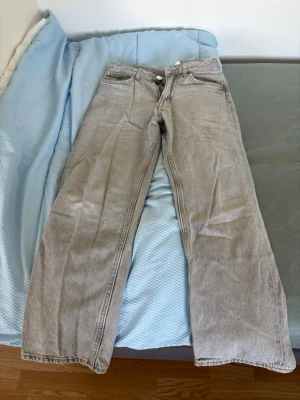 Grå raka jeans med hög midja - Säljer ett par grå jeans med raka ben och hög midja. Jeansen har klassisk femficksmodell, dragkedja och knapp i silverfärg. Materialet är denim i bomull och färgen är ljusgrå med en tvättad look. Perfekta för en avslappnad och trendig stil.