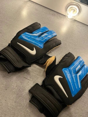 Nike målvaktshandskar  - Säljer ett par Nike målvaktshandskar i svart och blått med vita detaljer. Handskarna har kardborreband vid handleden .  Vid frågor skriv.