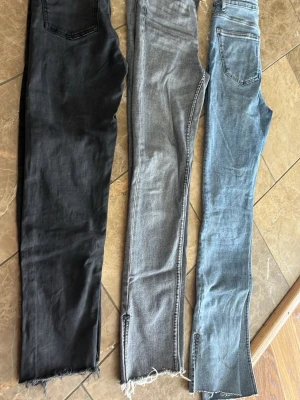 Tre par skinny jeans i olika färger - Säljer tre par skinny jeans i svart, grått och ljusblått. Alla har råa, fransiga benslut och klassisk femficksdesign. Jeansen är i stretchigt denimtyg och har smal passform som sitter tight längs benen. Perfekta för en trendig och avslappnad look.två från Zara en från Lindex 