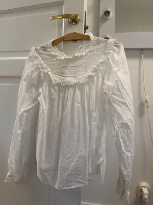 Vit blus med spets från & Other Stories - Romantisk vit blus från & Other Stories med lång ärm, hög krage och vackra spetsdetaljer. Blusen har broderade partier och volang vid halsen samt ärmslut. Perfekt för en chic och feminin look.