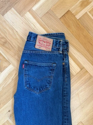 Levi's 501 jeans  - Klassiska blå jeans från Levi's med rak passform och hög midja. Jeansen har fem fickor, gylf med dragkedja och knapp samt den ikoniska läderlappen bak i midjan. Tillverkade i slitstark denim med snygg tvätt och röda Levi's-taggen på bakfickan.