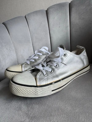 Silvriga sneakers med vita snören - Säljer ett par snygga sneakers i metallic silver med vita snören och vit sula. Skorna har klassisk låg modell med rund tå och svarta detaljer längs sulan. Perfekta för dig som vill sticka ut med en cool och modern stil.