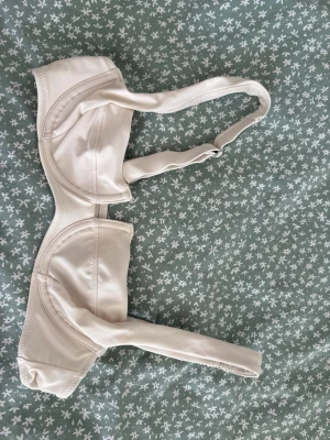 Beige bikiniöverdel med bygel XS - Snygg beige bikiniöverdel i enkel och stilren design. Överdelen har bygel för extra stöd och justerbara axelband. Perfekt för dig som vill ha en klassisk look på stranden eller vid poolen.