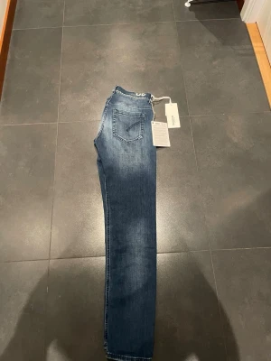 Blå slim fit jeans med fickor - Snygga blå slim fit jeans med klassisk femficksdesign och vita sömmar. Jeansen har en något tvättad look och normal midja. Materialet ser ut att vara stretchigt denim, vilket ger en bekväm passform. Perfekta för en trendig och avslappnad stil.