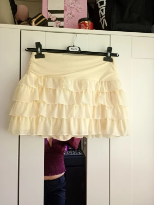 Ljus gul volangkjol med flera lager - Supersöt ljus gul kortkjol med flera lager volanger som ger en fluffig och lekfull look. Kjolen har en mjuk resår i midjan och är tillverkad i ett lätt, flowy material som känns bekvämt. Perfekt för dig som vill ha en feminin och trendig stil.💕
