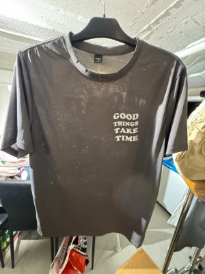 Grå t-shirt med tryck och blommor - Säljer en grå t-shirt med texten 'Good things take time' tryckt på både fram- och baksidan. Ena sidan har även ett stort blommotiv i svartvitt. T-shirten har rund hals och korta ärmar, perfekt för en avslappnad stil. Finns att hämta i Gröndal.
