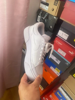 Nike Court Vision Alta Vita  - Snygga helvita sneakers med platåsula och klassisk snörning. Skorna har en stilren design med diskreta sömmar och en upphöjd sula som ger extra attityd. Tillverkade i syntetmaterial och passar perfekt till streetwear eller casual outfits.
