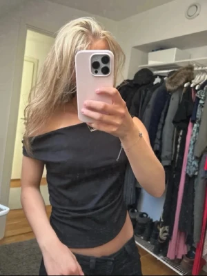 Svart offshoulder topp - Snygg svart offshoulder topp med asymmetrisk skärning och croppad passform. Toppen har en stilren look och är perfekt för dig som gillar trendiga detaljer. Materialet känns mjukt och följsamt mot kroppen.