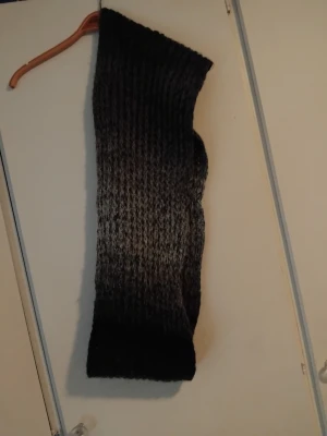 Mörkgrå stickad halsduk Alice Bizous - Säljer en lång och mysig mörkgrå stickad halsduk från Alice Bizous. Halsduken är gjord i 100% akryl och har ett grovt stickat mönster som ger en cool och avslappnad vibe. Perfekt för att hålla värmen under kalla dagar.