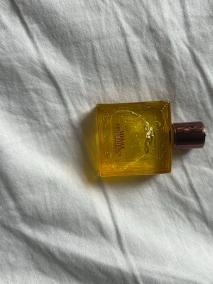 Versace Eros Energy EDP 5 ml - Versace Eros Energy Eau de parfum i en liten 5 ml flaska. Flaskan är fyrkantig och genomskinligt gul med ett elegant mönster och Versaces ikoniska Medusa-huvud på framsidan. Korken är metallic och har en kopparfärgad ton. Kommer med matchande gul kartong.