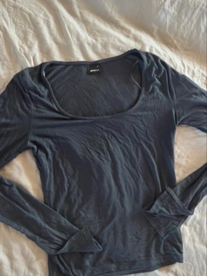Mörkblå långärmad topp - En enkel och stilren mörkblå långärmad topp med rundad, djup urringning. Tillverkad i ett mjukt och stretchigt material som sitter snyggt på kroppen. Perfekt att matcha med jeans eller kjol för en clean look.