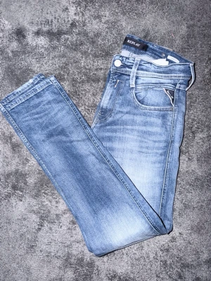Blå slim fit jeans från Replay - Snygga blå slim fit jeans från Replay med klassisk femficksmodell och ljusa slitningar på låren. Jeansen har normal midja, dragkedjegylf och raka ben. Perfekta för en avslappnad och trendig look. Storlek. W28 L32