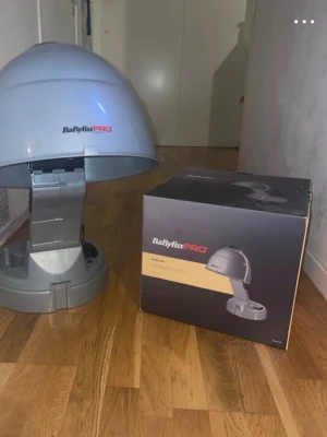 BaByliss PRO hårtorkhuv - Säljer en BaByliss PRO hårtorkhuv i grå plast med modern design. Perfekt för dig som vill fixa håret hemma med salongskänsla. Produkten har en rundad form och står stadigt på golvet. Levereras med originalkartong.