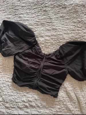 Svart croppad topp från H&M - Säljer en svart croppad topp från H&M med puffiga korta ärmar och dragkedja i sidan. Toppen har en snygg v-ringning och är gjord i bomull, perfekt för att lyfta vilken outfit som helst.