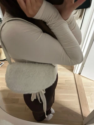 Vit fluffig axelväska - Säljer en supermjuk och fluffig vit axelväska i fuskpäls. Väskan har en enkel rektangulär form och ett vitt axelband. Perfekt för dig som vill ha en trendig accessoar med cozy känsla.
