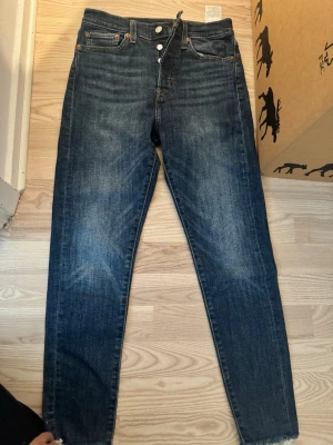Mörkblå Levis  jeans - Säljer ett par mörkblå Wedgie Skinny jeans med hög midja och knappgylf. Jeansen har klassisk femficksdesign, kontrastsömmar och snygg tvätt med slitningar på låren. Perfekta för dig som gillar en smal passform och tidlös denimstil.