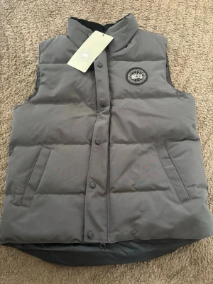 Canada Goose väst helt ny med lappar kvar! -  Säljer en snygg Canada Goose-väst i helt nytt skick. Västen är aldrig använd och alla originaletiketter och lappar sitter fortfarande kvar. Perfekt för dig som vill ha en stilren och varm väst av hög kvalitet.
