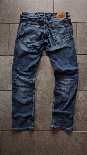 Replay Anbass - Säljer ett par blå jeans från Replay med snygga slitningar och tvättade detaljer. Klassisk femficksmodell med dragkedja och knapp i midjan. Jeansen har en normal passform och är perfekta för en avslappnad stil.