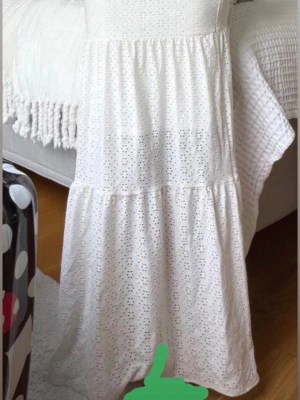 Vit långklänning med broderad spets - Vit långkjol i bomull med broderade hålmönster och volang. Kjolen har en luftig och flowy passform, perfekt för varma dagar.