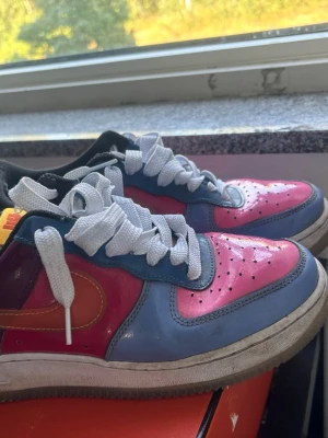 UNDFTD Nike Air Force 1 sneakers - Säljer ett par Nike Air Force 1 sneakers i en riktigt färgstark kombo med rosa, blå, lila och orange detaljer. Skorna har vit snörning, klassisk låg siluett och en robust sula. Perfekta för dig som vill sticka ut med din stil.
