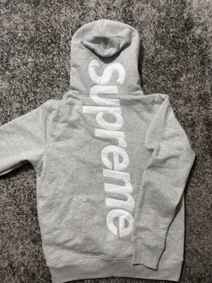 Gråa Supreme hoodie  - Hej! Säljer min gråa Supreme hoodie. Stor vit text på ryggen, bra skick. Har använts men ser fortfarande fin ut. Hör av dig om du vill ha de. Perfekt inför vintern som börjar närma sig. Storlek-S. Skick-mycket bra. Om du är intresserad eller har några frågor, bud är det bara att höra av er!!!