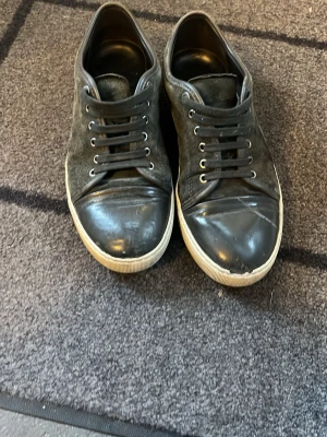 Svarta Lanvins  - Snygga svarta sneakers från Lanvin med ovandel i mocka och tåparti i blankt läder. Skorna har vita sulor och klassisk låg profil med svarta skosnören. Perfekta för en stilren och avslappnad look.