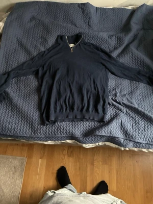 Mörkblå stickad tröja med halv dragkedja - Mörkblå stickad tröja med halv dragkedja i halsen och ribbade muddar vid ärmslut och nederkant. Tröjan har lång ärm och en klassisk, enkel design som passar till mycket. Materialet ser mjukt och bekvämt ut. Den kan även passa xxl 