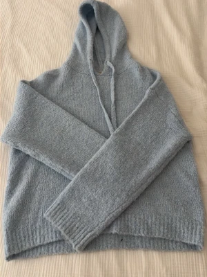 Ljusblå stickad hoodie - Mysig ljusblå stickad hoodie med huva och dragsko. Tröjan har långa ärmar och ribbade muddar vid ärmslut och nederkant. Perfekt för dig som gillar en avslappnad och chill stil. Materialet känns mjukt och skönt mot huden. Använd ett fåtal gånger 