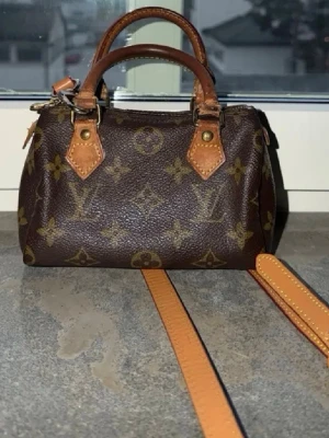 Louis Vuitton brun monogram handväska - Säljer en klassisk brun handväska från Louis Vuitton med det ikoniska monogrammönstret. Väskan har två korta handtag i läder och en avtagbar axelrem i ljusbrunt läder. Perfekt storlek för det viktigaste och en tidlös design.