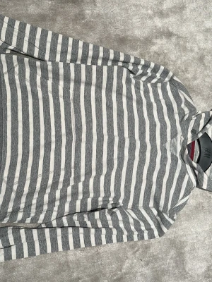 Gråvit randig hoodie  - Snygg hoodie från banana republic med grå och vita horisontella ränder, huva och känguruficka framtill. Tillverkad i mjukt bomullsmaterial och har ribbade muddar vid ärmslut och nederkant. Perfekt för en avslappnad och stilren look.