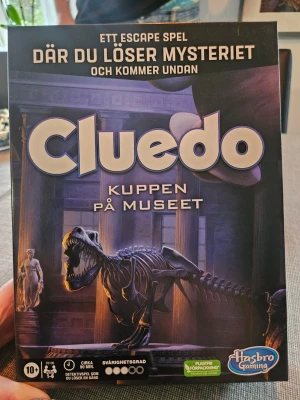 Cluedo Kuppen på Museet sällskapsspel - Cluedo Kuppen på Museet är ett escape-spel där du löser mysterier och samarbetar för att fly från museet och fånga förrädaren. Spelet har en dynamisk spelplan, ledtrådskort och olika karaktärer. Passar för 1-6 spelare och rekommenderas från 10 år. Vi har spelat spelet en gång och därför är kassaskåpet öppet men det ligger bara en detalj till spelet och påverkar ingenting Allt annat är en nyskick, man ser inte att spelet är spelat förutom att den pappersförseglingen är bruten
