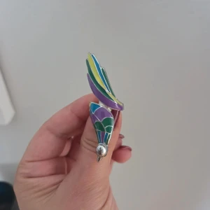 Unik färgglad ring med emaljdetaljer – Helt ny! - Säljer en supersnygg och iögonfallande ring med detaljer i lila, grönt, blått och gult. Ett riktigt statement-smycke som piffar upp vilken outfit som helst! Design: Konstnärlig och unik form med emaljerade färger och silverfärgade detaljer.Helt ny och aldrig använd. Kan skickas med frimärke för 15 kr eller spårbart, säg till innan köp! Samfraktar gärna. 🌸
