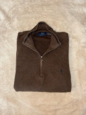 Brun halvzip tröja från Polo Ralph Lauren - Säljer en brun stickad tröja från Polo Ralph Lauren med halv dragkedja och hög krage. Tröjan är XL men jag som vanligtvis använder L har aldrig trott att det är en L tröja. Tröjan har lång ärm, ribbade muddar och den klassiska broderade loggan på bröstet. Perfekt för lager på lager