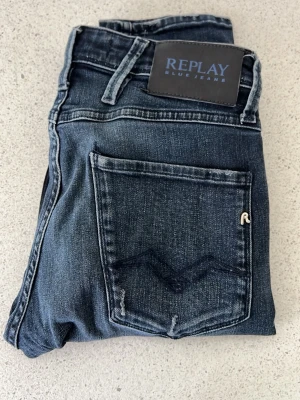 Replay anbass  - Snygga mörkblå jeans från Replay i modellen Anbass. Klassisk femficksdesign med detaljerad bakficka och Replay-logga på linningen. Jeansen har en tvättad look och raka ben. Perfekta för en trendig och avslappnad stil. En liten slitning vid knät. W27 L32