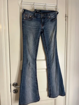 Blå bootcut jeans med kontrastsömmar, lågmidjade - Säljer ett par blå bootcut jeans med snygga kontrastsömmar och broderade bakfickor. Jeansen har låg midja, klassisk femficksdesign och utsvängda ben. 