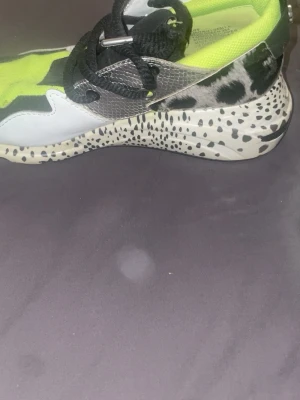 Sneakers med neon och djurmönster - Unika sneakers med neonfärgade detaljer, svart och vitt djurmönster på hälen och sulan samt svarta skosnören. Ovandelen är i mesh och syntetmaterial i svart, vitt och limegrönt. Snygg och modern design som sticker ut.