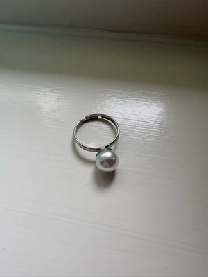 Silverfärgad ring med pärldetalj - Stilren ring i silverfärgad metall med en stor vit pärla som detalj. Ringen har en minimalistisk design.
