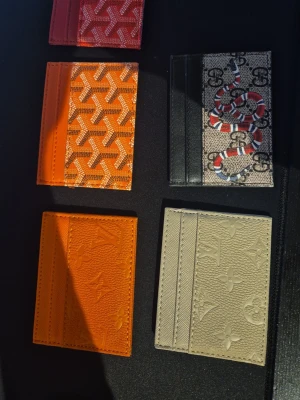 Färgglada kortfodral i läder - Fem stilrena kortfodral i olika färger och mönster. Två med klassiskt monogrammönster i orange och beige, två med grafiskt mönster i rött och orange samt ett med ormmotiv på beige och svart bakgrund. Alla är tunna och smidiga, perfekta för kort och ID. (Kan köpa olika också)
