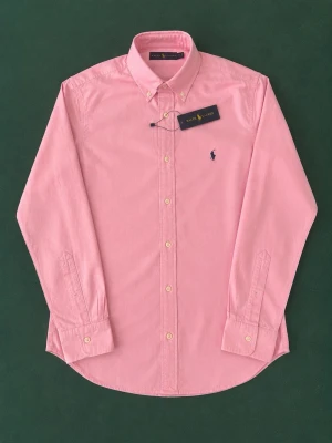 Rosa skjorta från Ralph Lauren - Klassisk rosa skjorta från Ralph Lauren med button-down krage och broderad logga på bröstet. Skjortan har långa ärmar, vita knappar och är tillverkad i mjuk bomull. Perfekt för en stilren och avslappnad look.