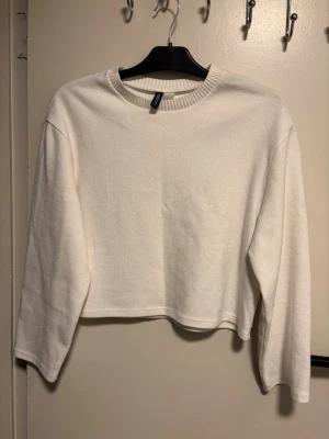 Vit croppad tröja från H&M Divided - Säljer en enkel och stilren vit croppad tröja från H&M Divided. Tröjan har långa ärmar, rund halsringning med ribbad kant och är gjord i ett mjukt material. Perfekt att matcha med höga jeans eller kjol.