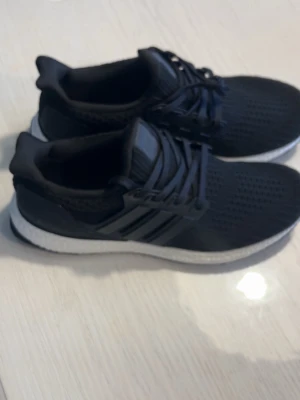 Adidas ultra boost - Snygga svarta sneakers med stickad ovandel och vita sulor. Skorna har svarta snören och tre ränder på sidan. Perfekta för en sportig och stilren look. Ovandelen är i mesh-liknande material för bra andningsförmåga.