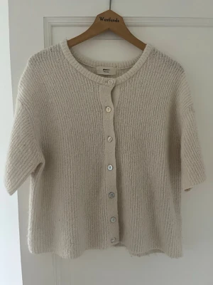 Beige kortärmad kofta Gina Tricot - Mysig beige kofta från Gina Tricot i ullblandning. Kortärmad modell med rund halsringning och knappar framtill. Perfekt att slänga över en topp för en avslappnad men ändå stilren look.