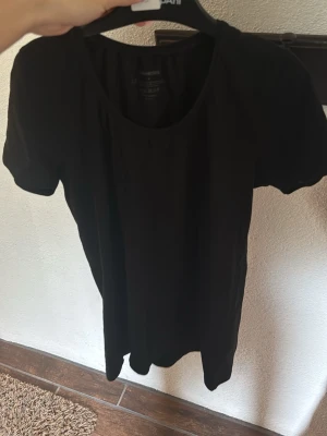 Svart basic t-shirt med rund hals - En enkel svart t-shirt med rund halsringning och korta ärmar. Perfekt till alla outfits och gjord i mjuk bomull för skön känsla. Passformen är normal och modellen är klassisk utan några extra detaljer.